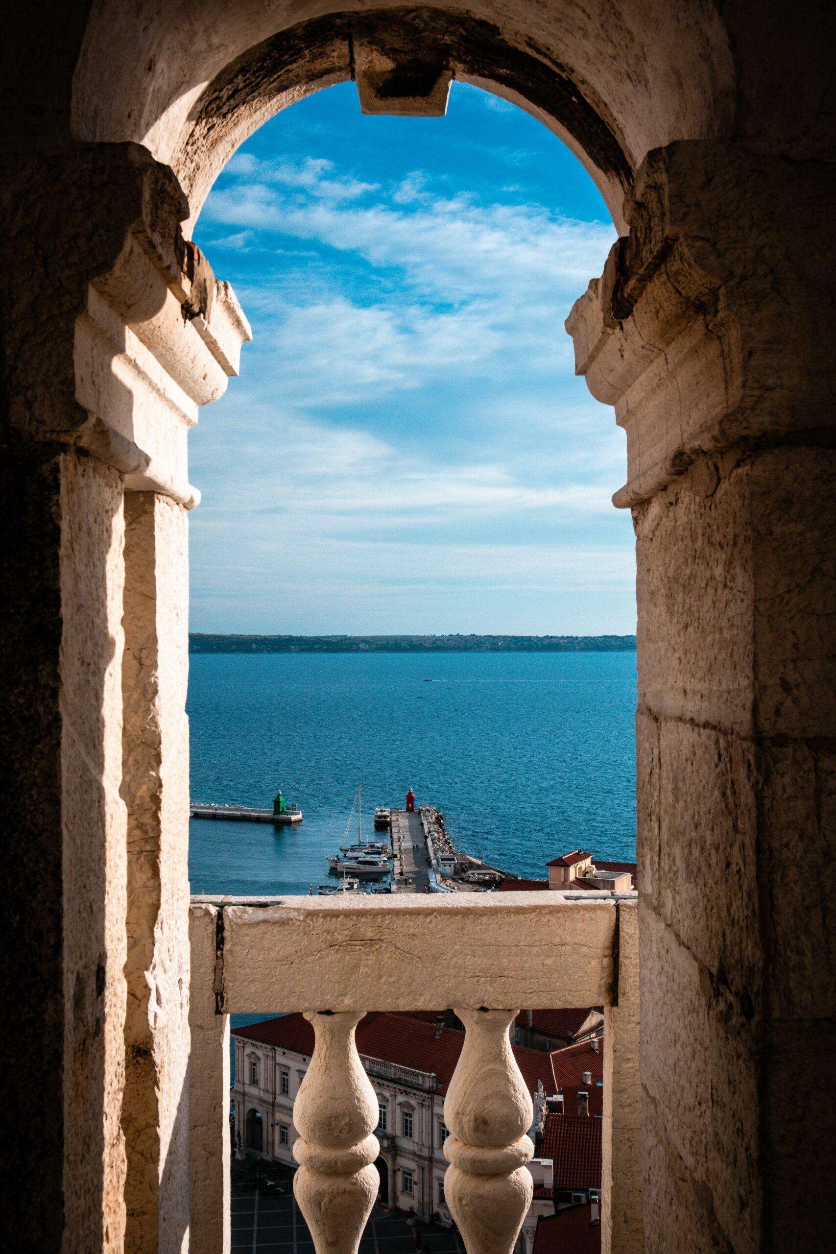Scenic view of a coastal pier through an old stone arch, showing blue sea and sky.