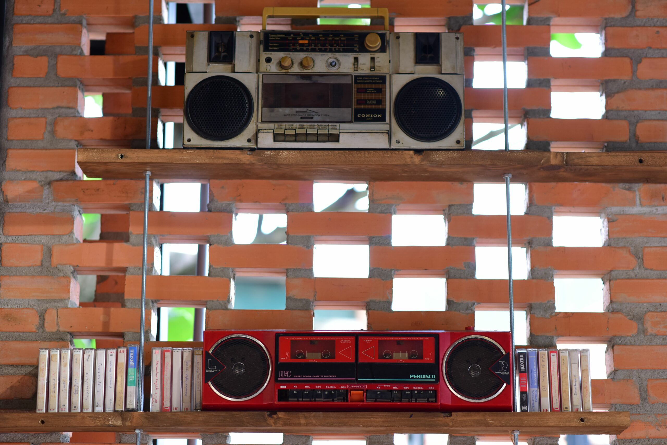 Two vintage radios and audio cassettes displayed on rustic wooden shelves against a brick wall.
