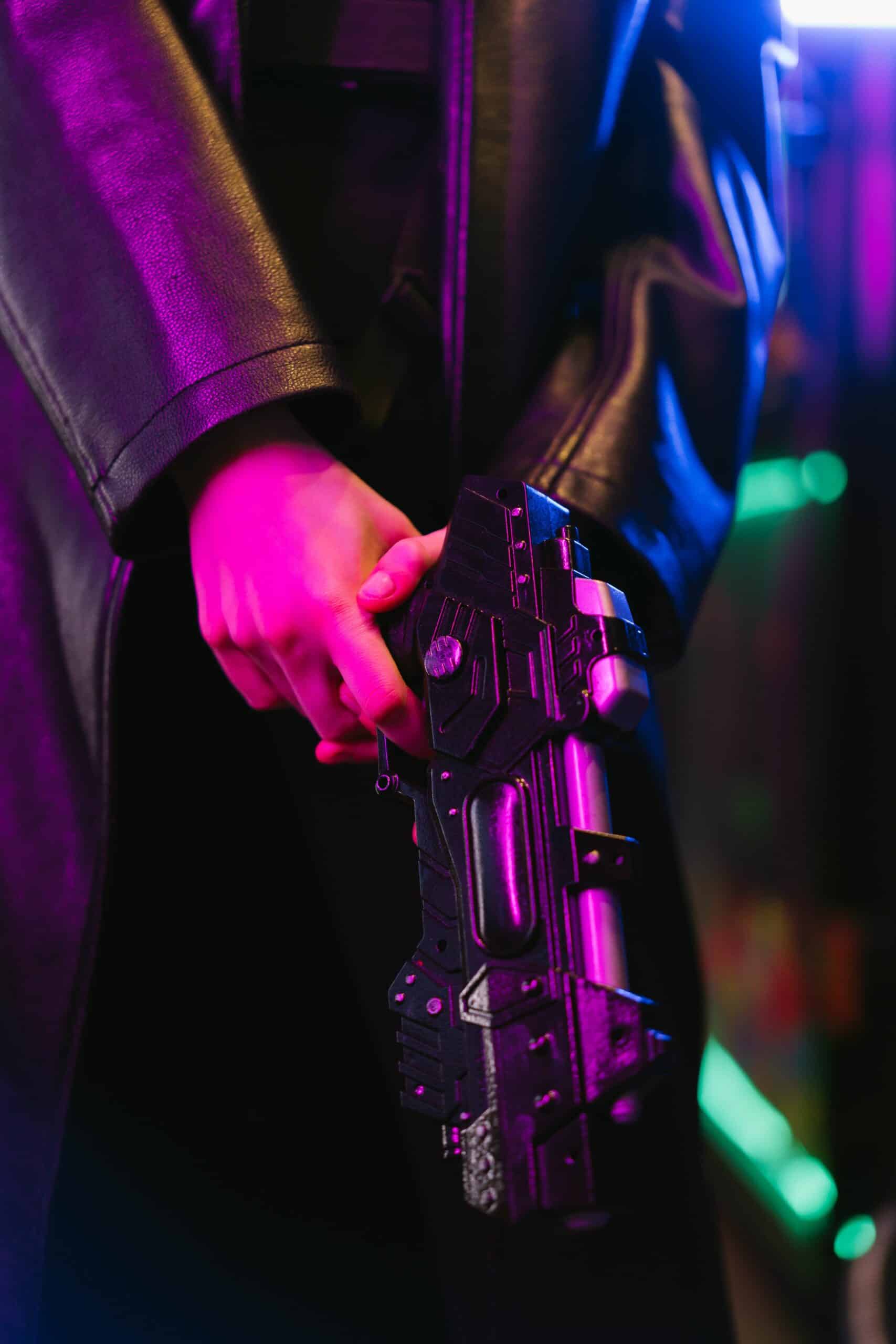A futuristic cyberpunk-themed image with a hand gripping a high-tech weapon in vibrant neon lighting.