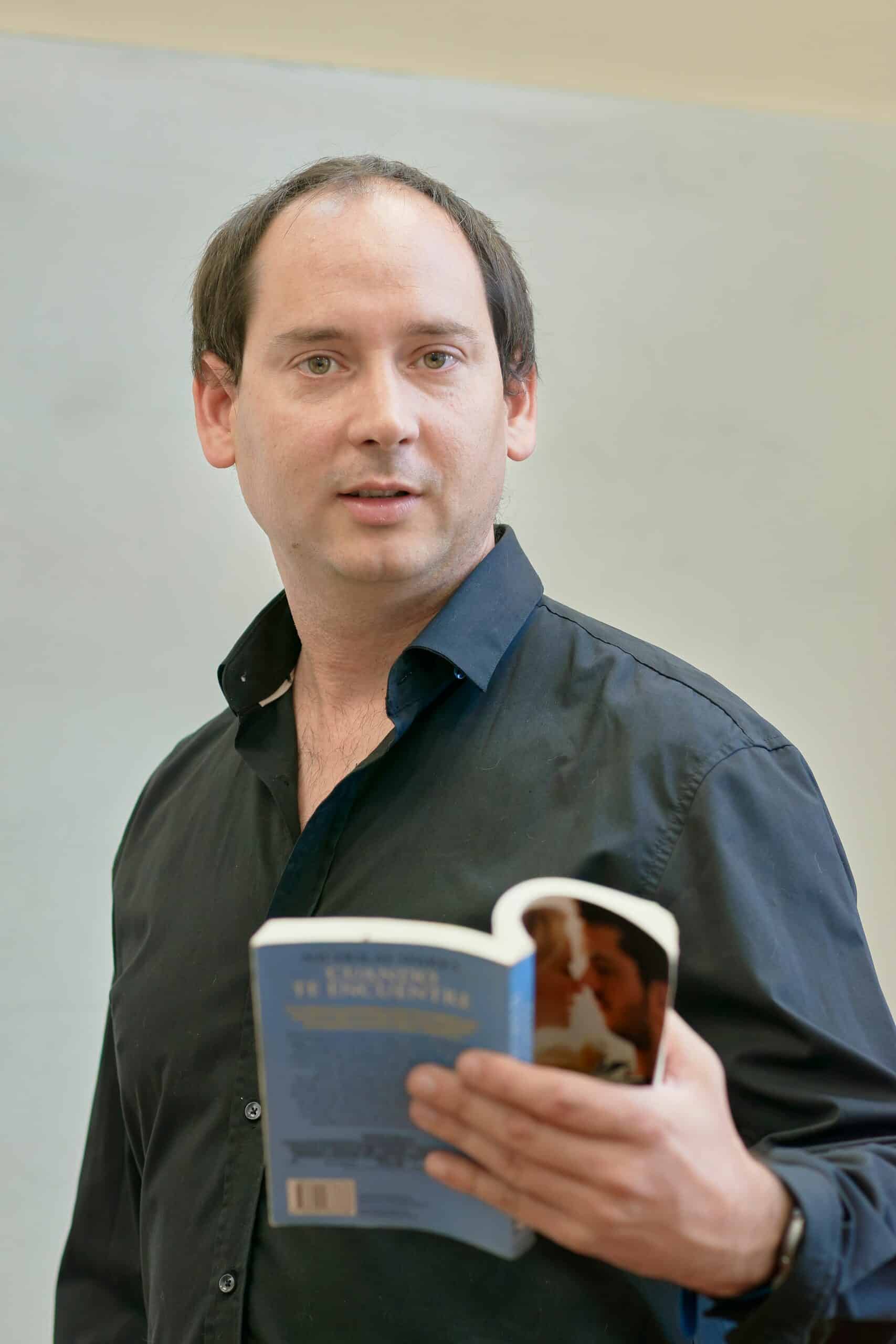 Adult man in classroom holding a book, engaging in a lecture or reading session.